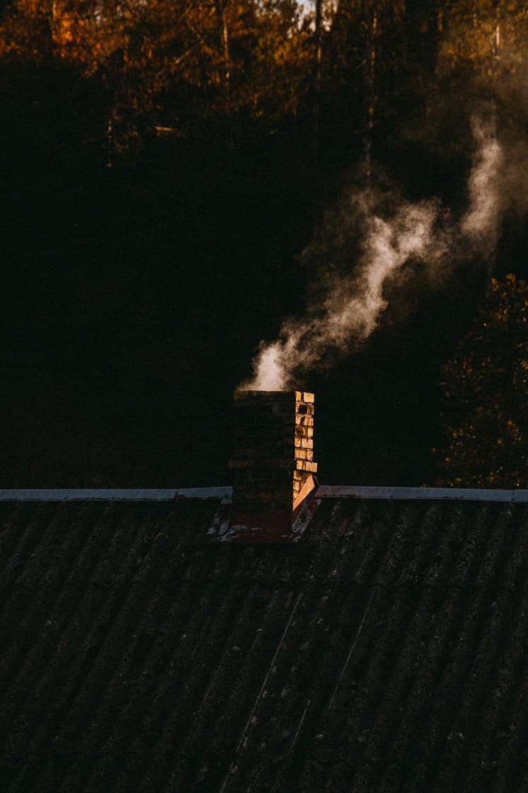 Cheminée de brique qui fume sur un toit, au crépuscule